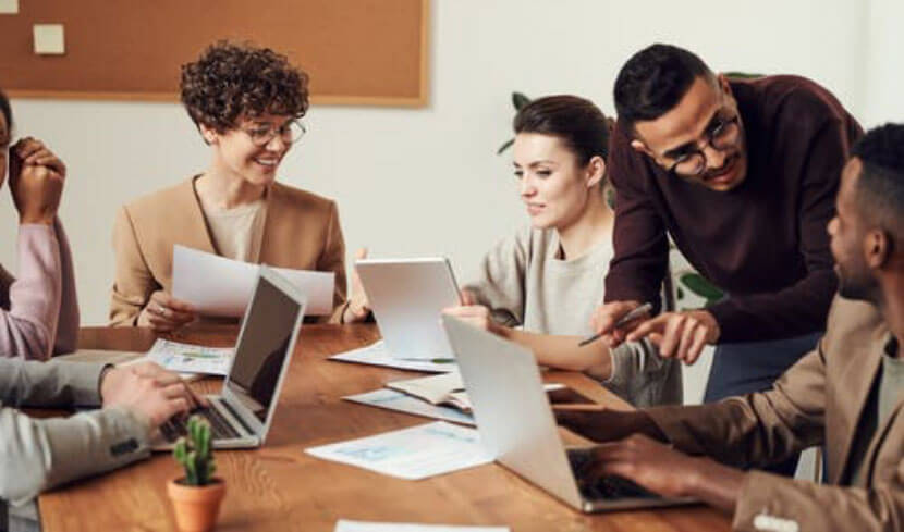 six people in a meeting with laptops and papers on the table