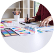 A person sits at a desk, working on color swatches and design sketches, in a brightly lit room.