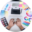 Overhead view of a graphic designer's workspace with hands typing, surrounded by color swatches and digital devices.