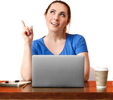 Woman in blue shirt sits at desk with a laptop, notebook, pen, and coffee cup, looking thoughtful and pointing upwards.