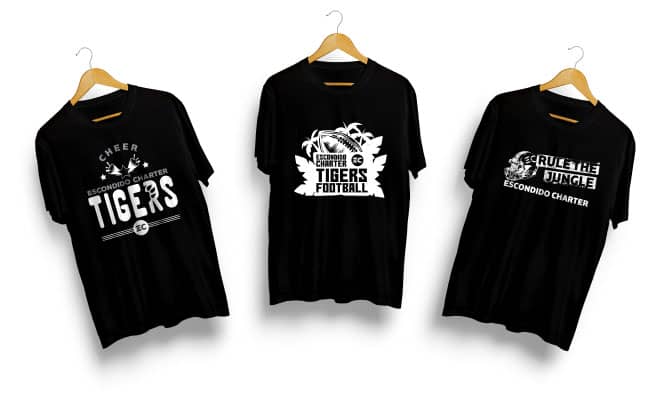 Three black T-shirts with different Escondido Charter sports team designs: Cheer Tigers, Tigers Football, and Rule The Jungle Tigers. All shirts are hanging on wooden hangers against a white background.